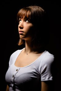 Portrait d'une jeune fille sur fond noir, de profil, regardant vers le haut.